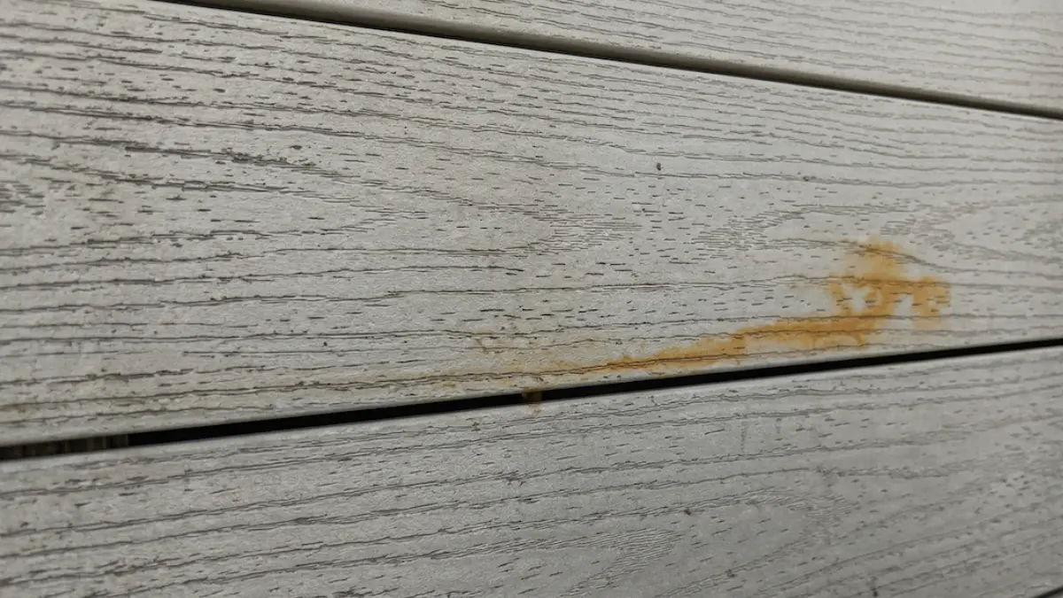 Close-up image of gray composite decking featuring yellowish-orange streaks, illustrating the wear and staining that homeowners use fake carpenter bee plugs to cosmetically repair and prevent in outdoor wood structures. Fake carpenter bee plugs causing rust stains on wood